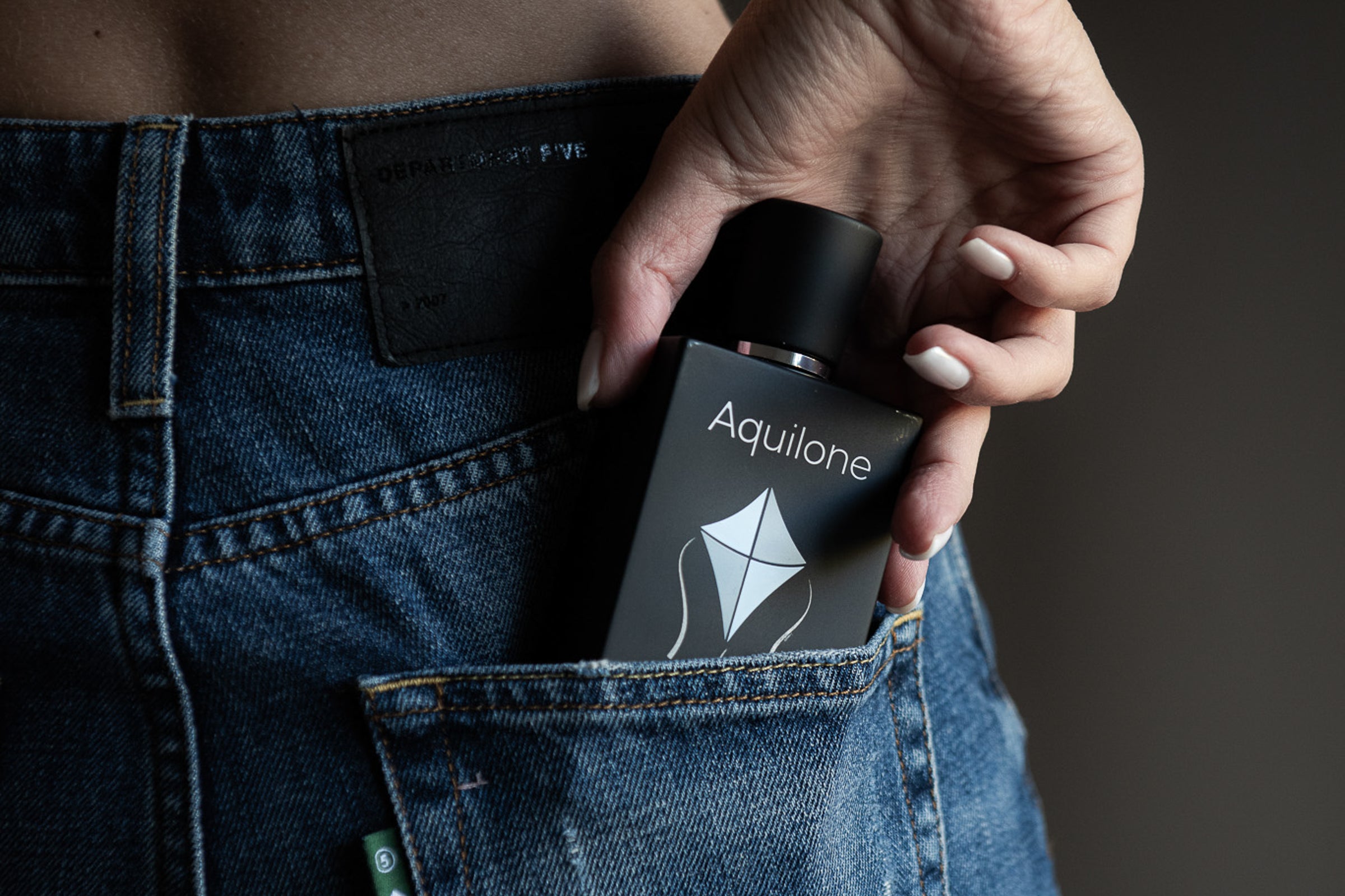 Hand zieht schwarzen matten Parfumflakon Caterina von Allegro mit geometrischem Logo aus der Gesäßtasche einer Jeans