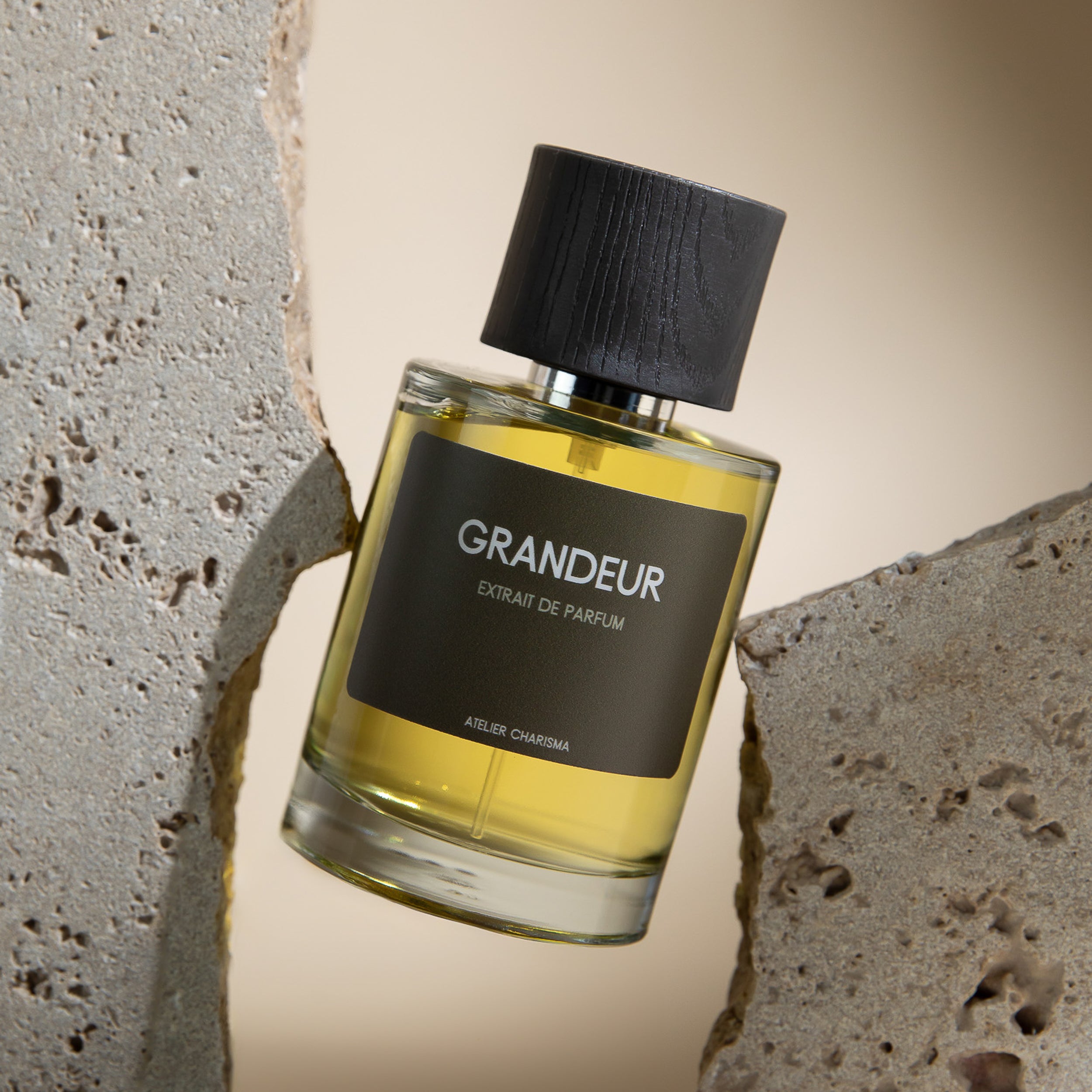 Parfumflakon Gandeur von Atelier Charisma mit goldener Flüssigkeit und strukturiertem Holzdeckel zwischen grauen Steinen auf hellem Hintergrund