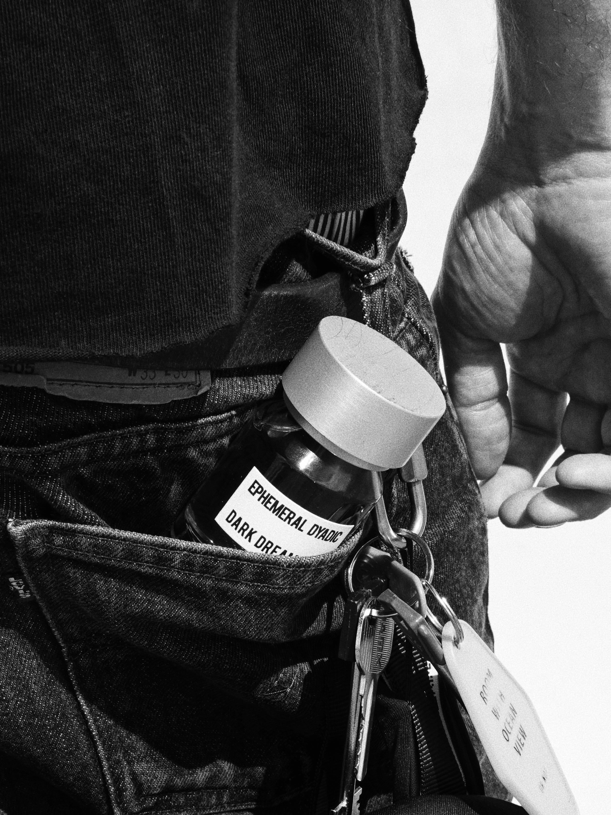 Parfumflakon Dark Dreams von Ephemeral Dyadic mit hellem Deckel in Jeanstasche, Karabiner mit Schlüsselbund an Gürtelschlaufe, schwarz-weiß
