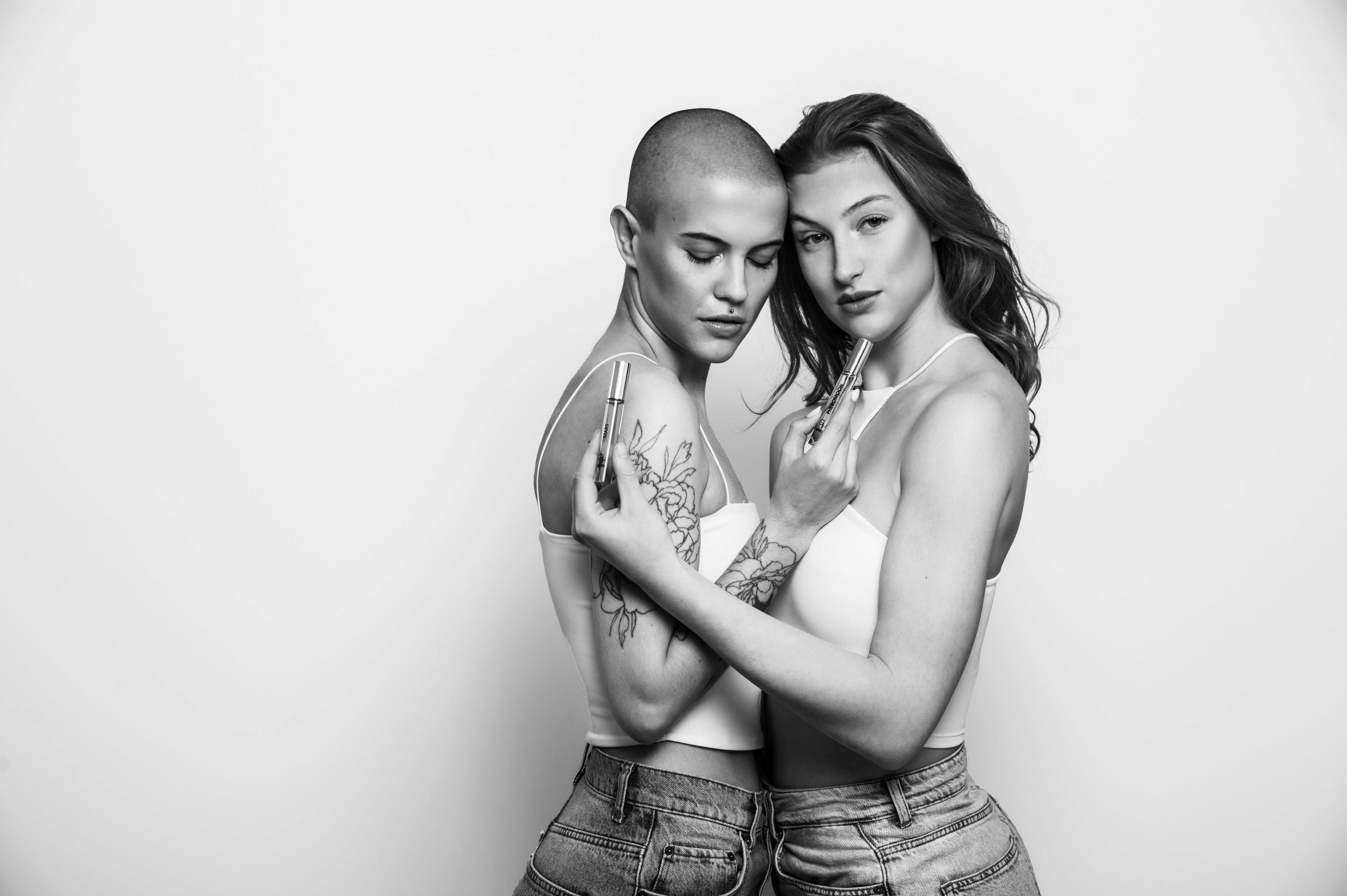 Schwarz-weiß Porträt zweier umarmter Frauen mit Sentir Duftöl Rollern von Goldenhand, eine mit rasiertem Kopf und Tattoos, die andere mit langen Haaren