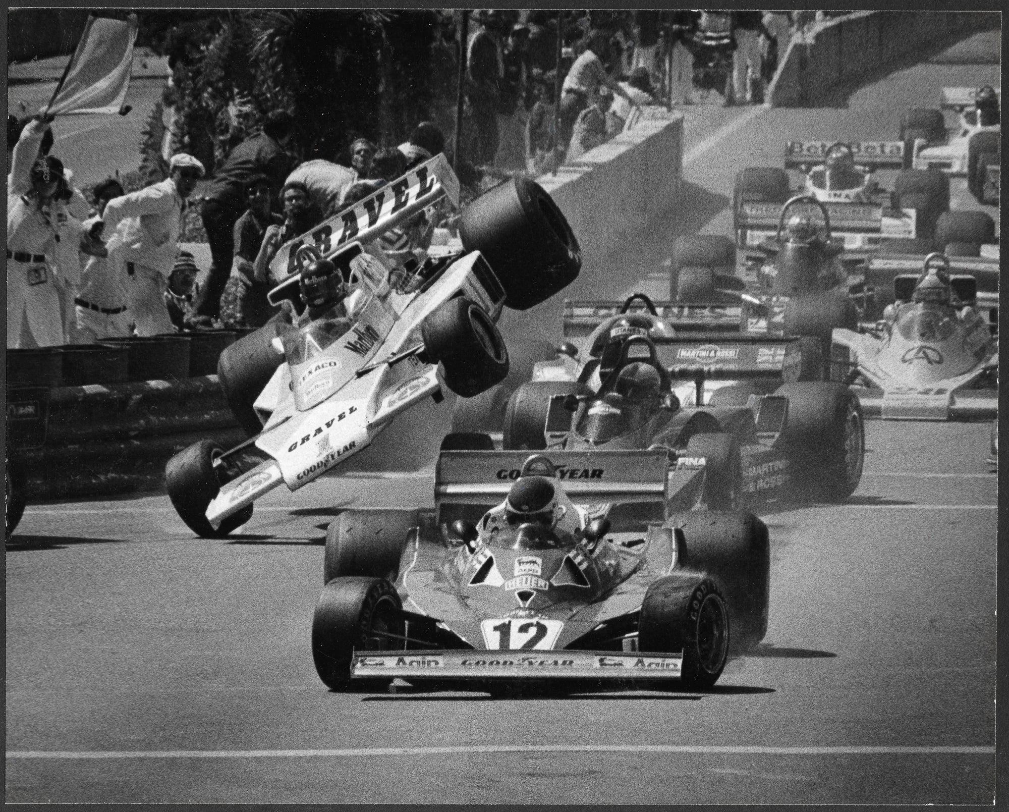 Schwarz-weiß Aufnahme eines dramatischen Formel-1-Unfalls mit fliegendem Rennwagen über anderen Fahrzeugen auf der Strecke, Zuschauer im Hintergrund