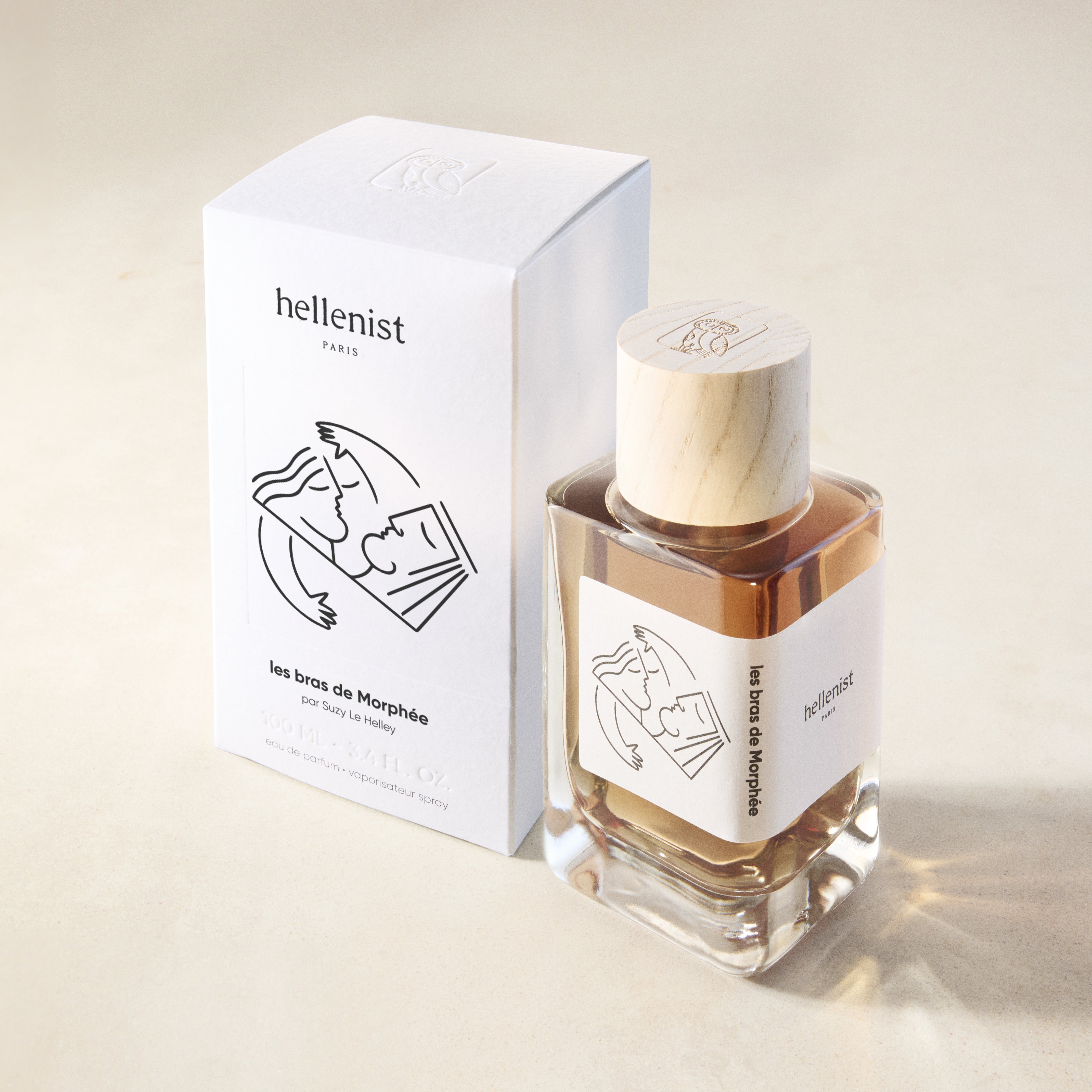 Parfumflakon Les bras de Morphée von Hellenist mit Holzdeckel und minimalistischer Linienzeichnung neben weißer Verpackung auf beigem Hintergrund