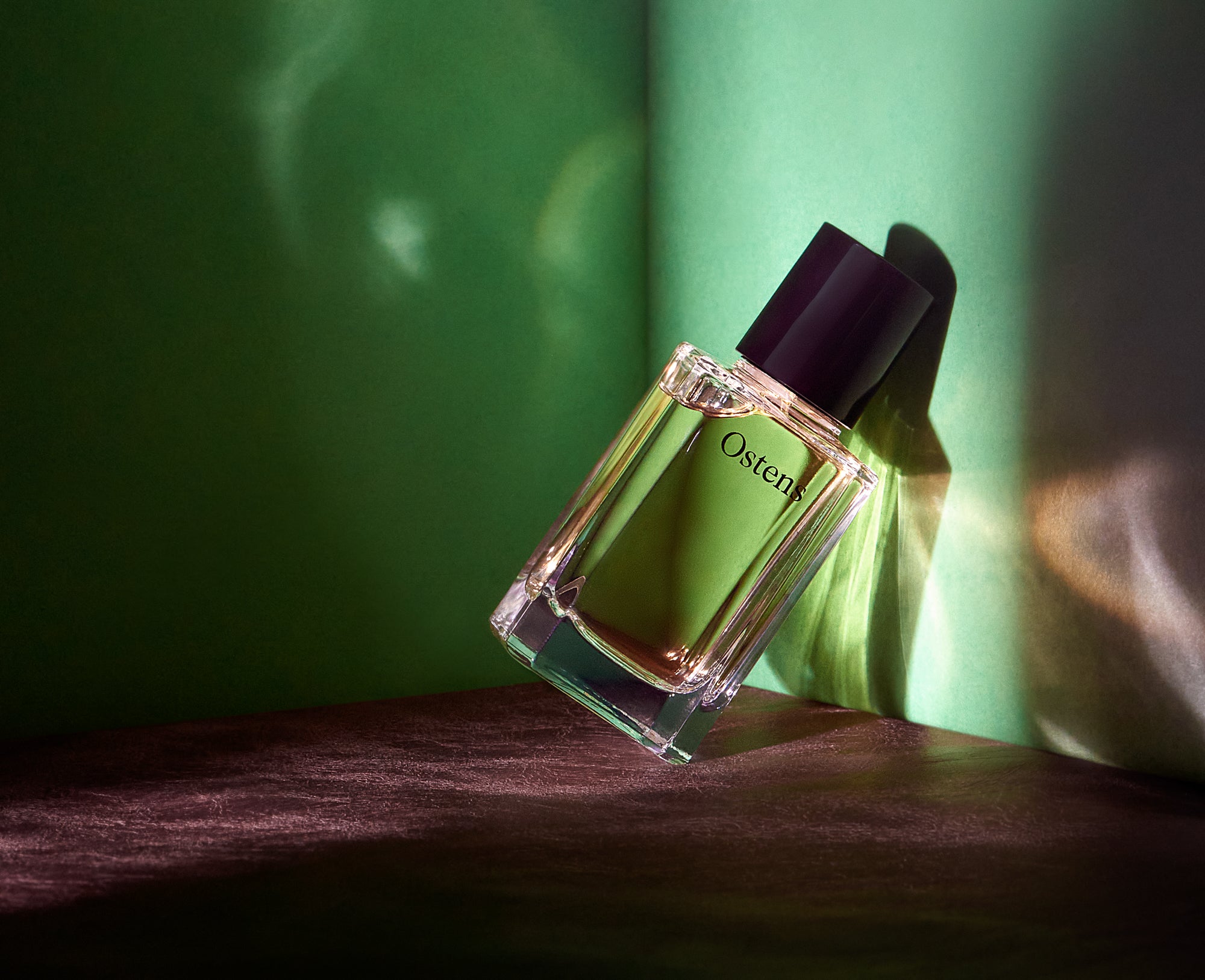 Parfumflakon Patchouli Heart No. 1 von Ostens mit transparenter Flüssigkeit und schwarzem Verschluss auf Holzoberfläche mit Flakonschatten, atmosphärisch ausgeleuchtet