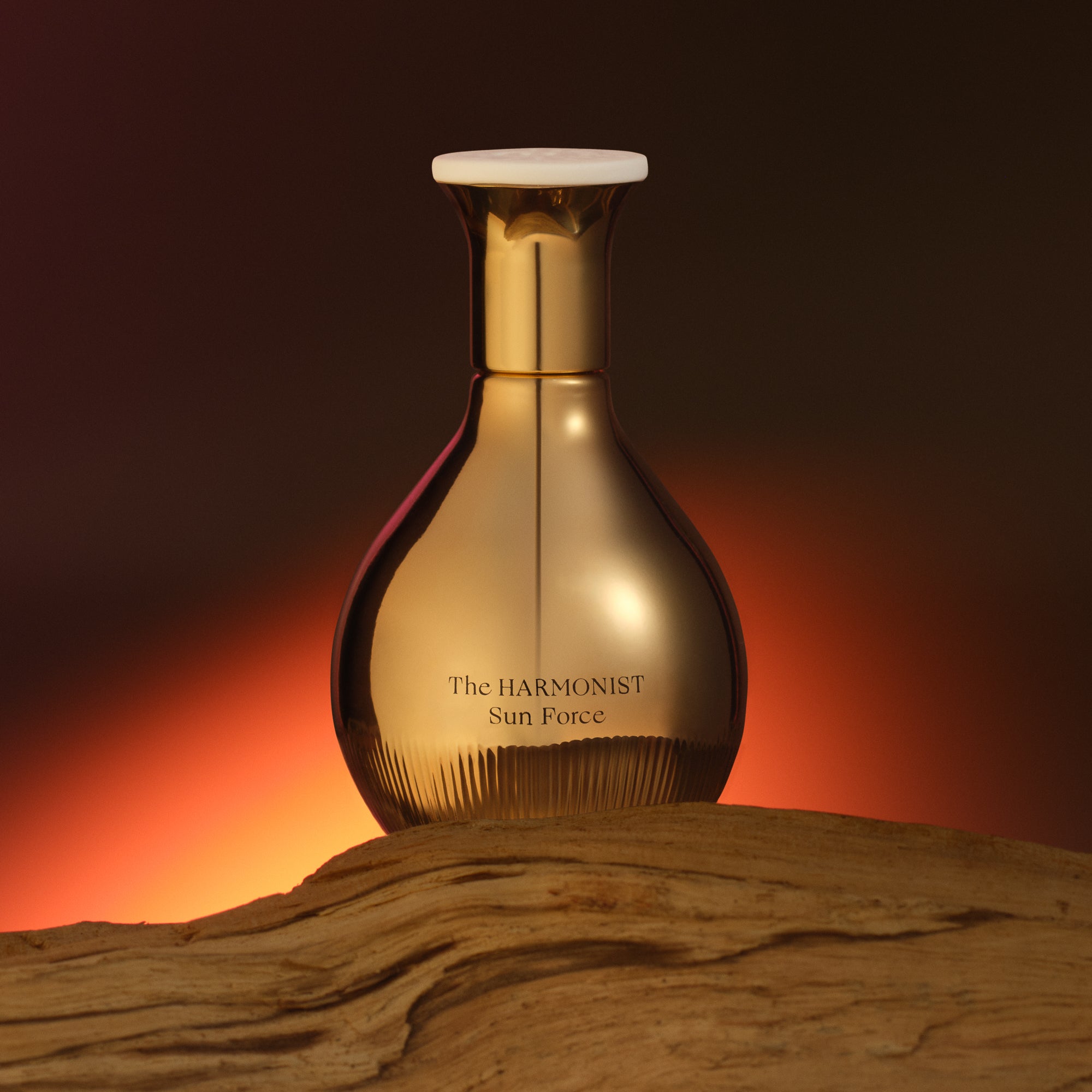 Parfumflakon Sun Force von The Harmonist mit goldenem bauchigen Glas und cremefarbenem Verschluss auf Holzoberfläche vor orange-rotem Hintergrund