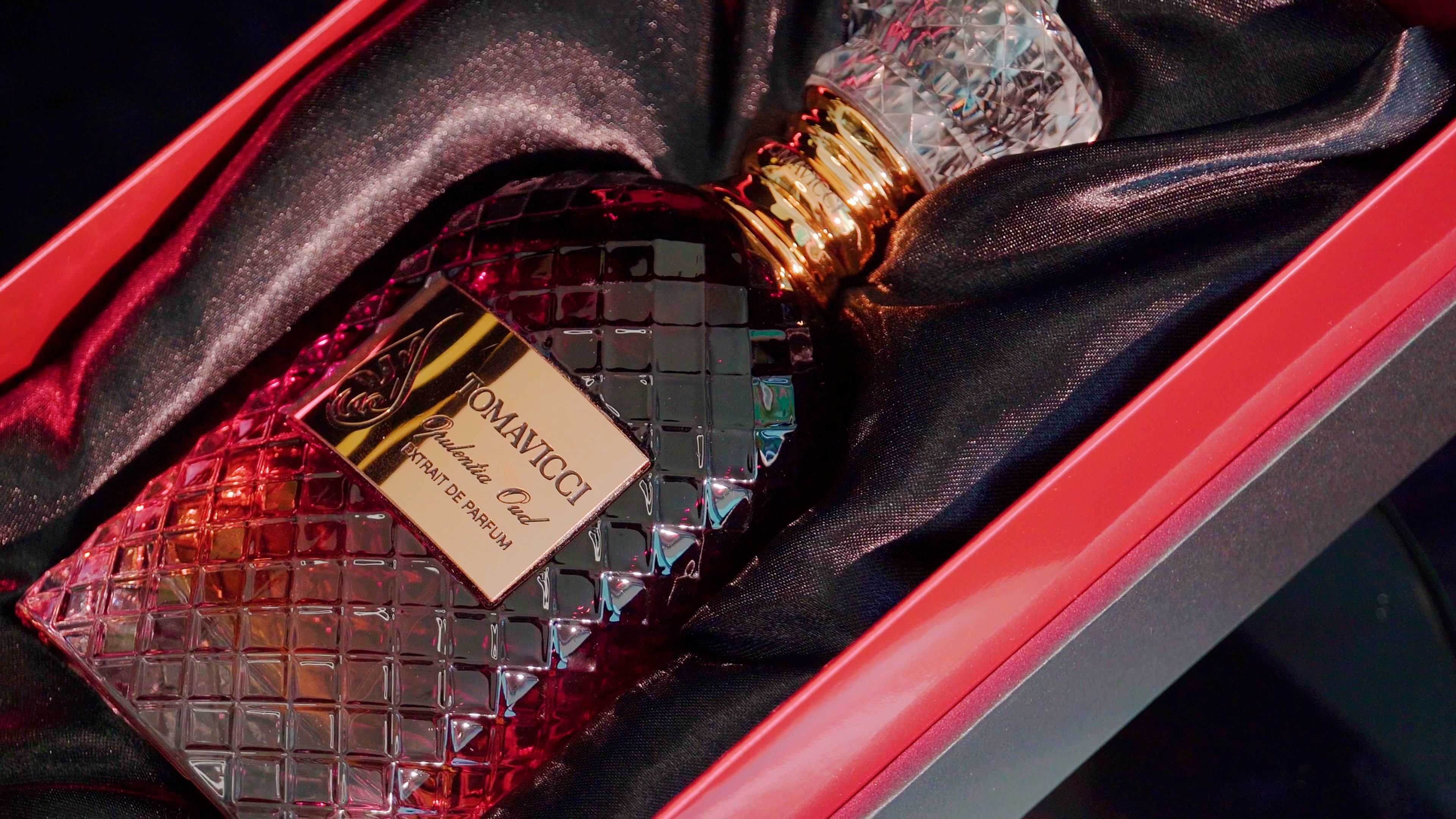 Parfumflakon Opulentia Oud von Tomavicci mit facettiertem Kristallglas, goldfarbenem Hals und kristallinenem Verschluss auf schwarzem Samt mit roten dekorativen Elementen
