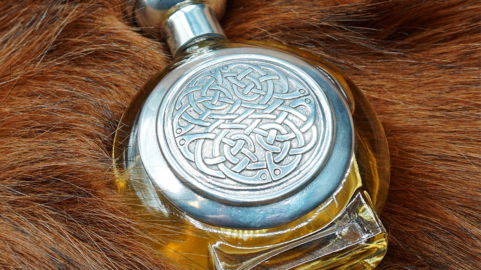 Parfumflakon von Boadicea the Victorious mit ornamentalem keltischem Knotenmuster als Metallplakette, auf braunem Fell