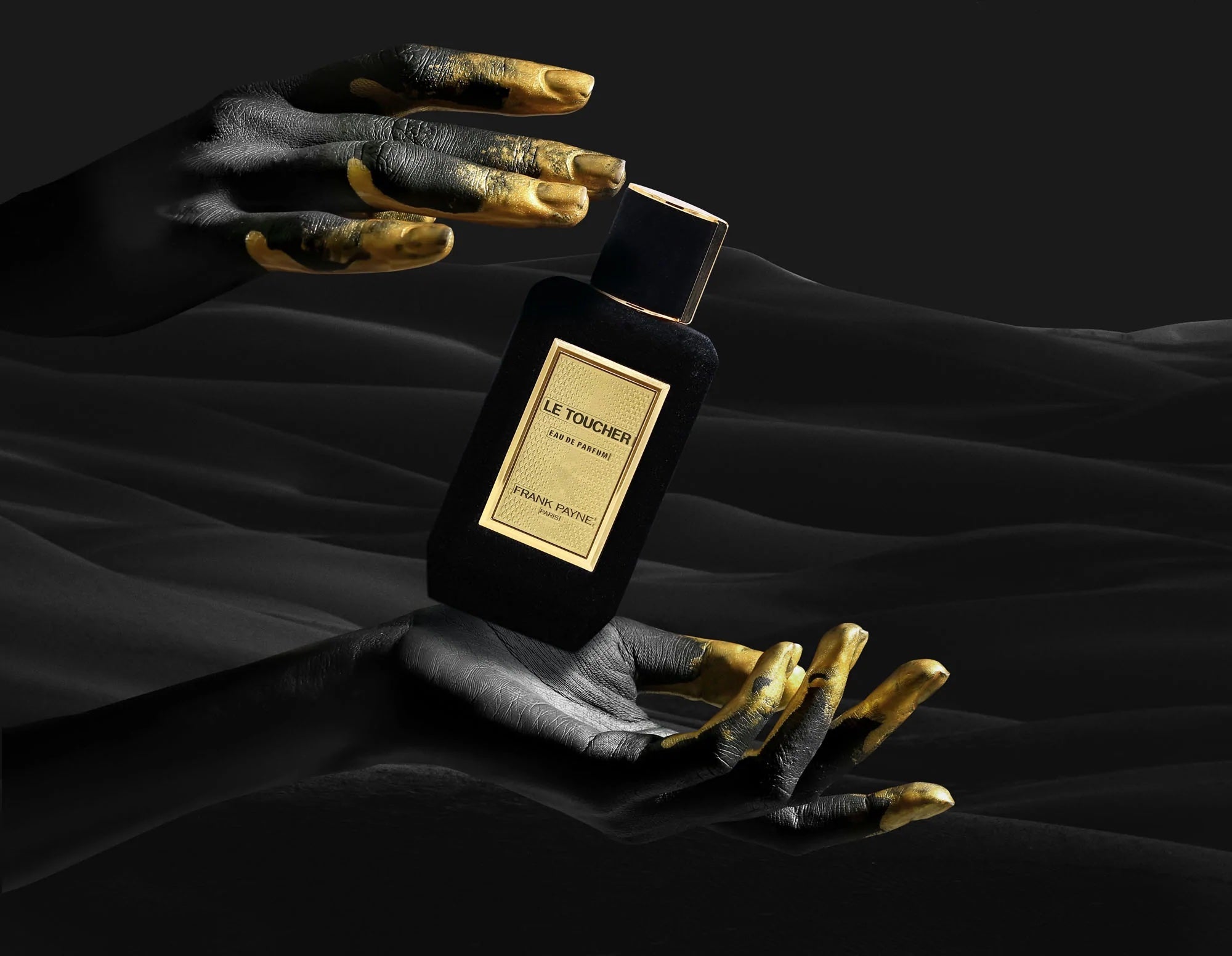 Samtüberzogener Parfumflakon Le Toucher von Frank Payne mit goldenem Etikett, gehalten von schwarz bemalten Händen mit goldenen Fingerspitzen