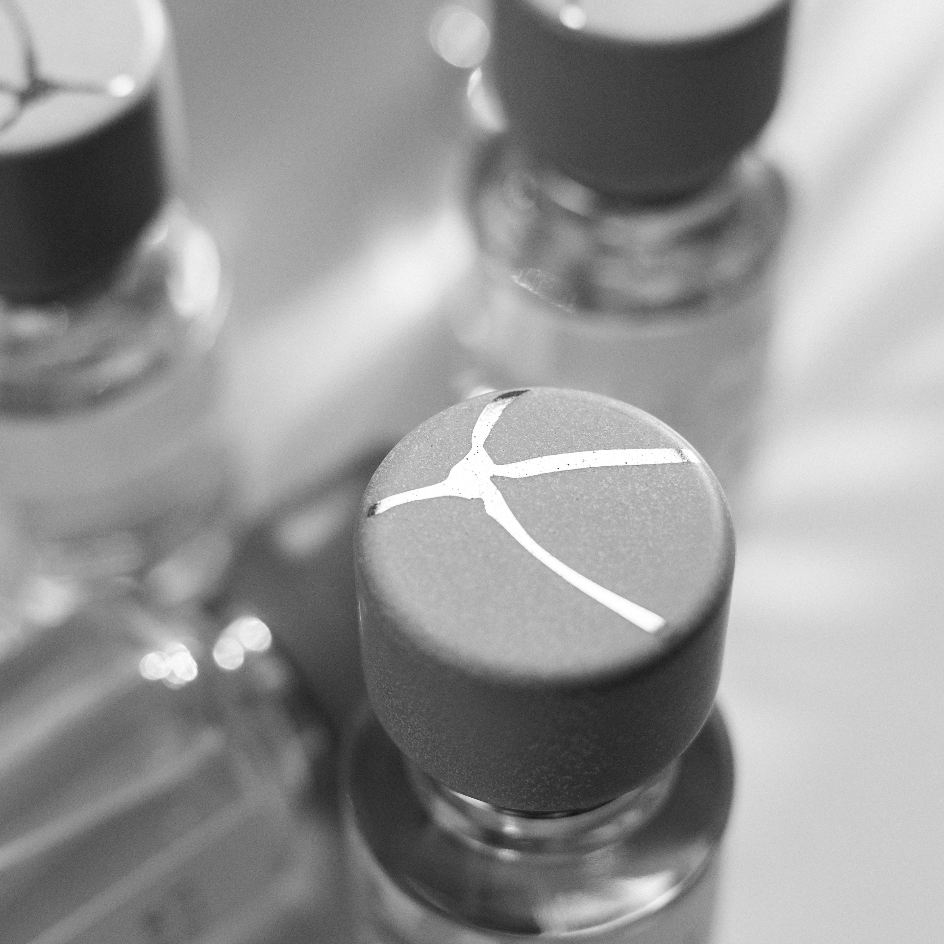 Schwarz-weiß Aufnahme von Parfumflakon der Marke L'eau Maliz mit minimalistischem Logo auf dem Deckel, weitere Flakons unscharf im Hintergrund