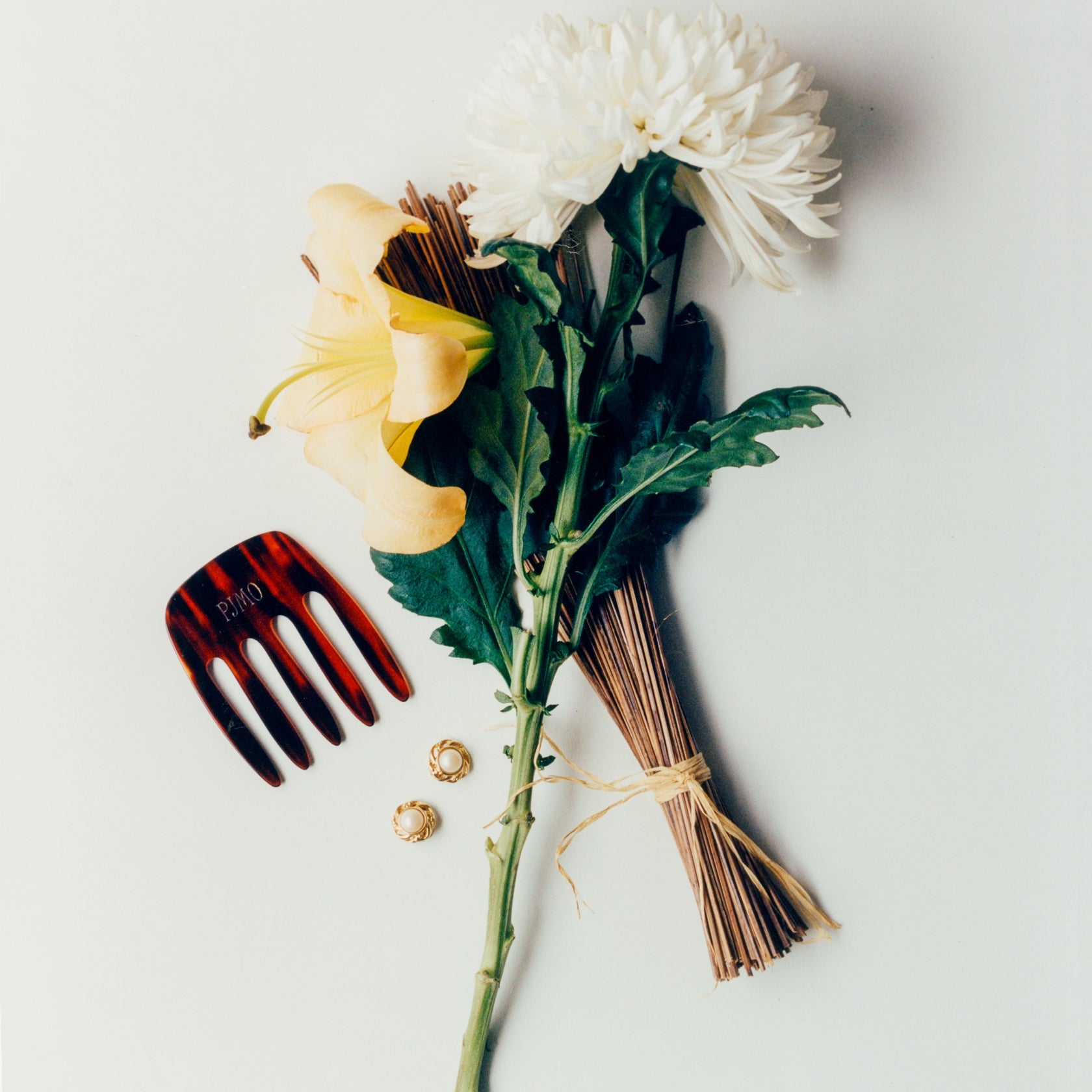 Liegendes Stillleben mit weißen und gelben Blumen, Räucherstäbchen, Schildpatt-Kamm und goldenen Ohrringen auf hellem Hintergrund