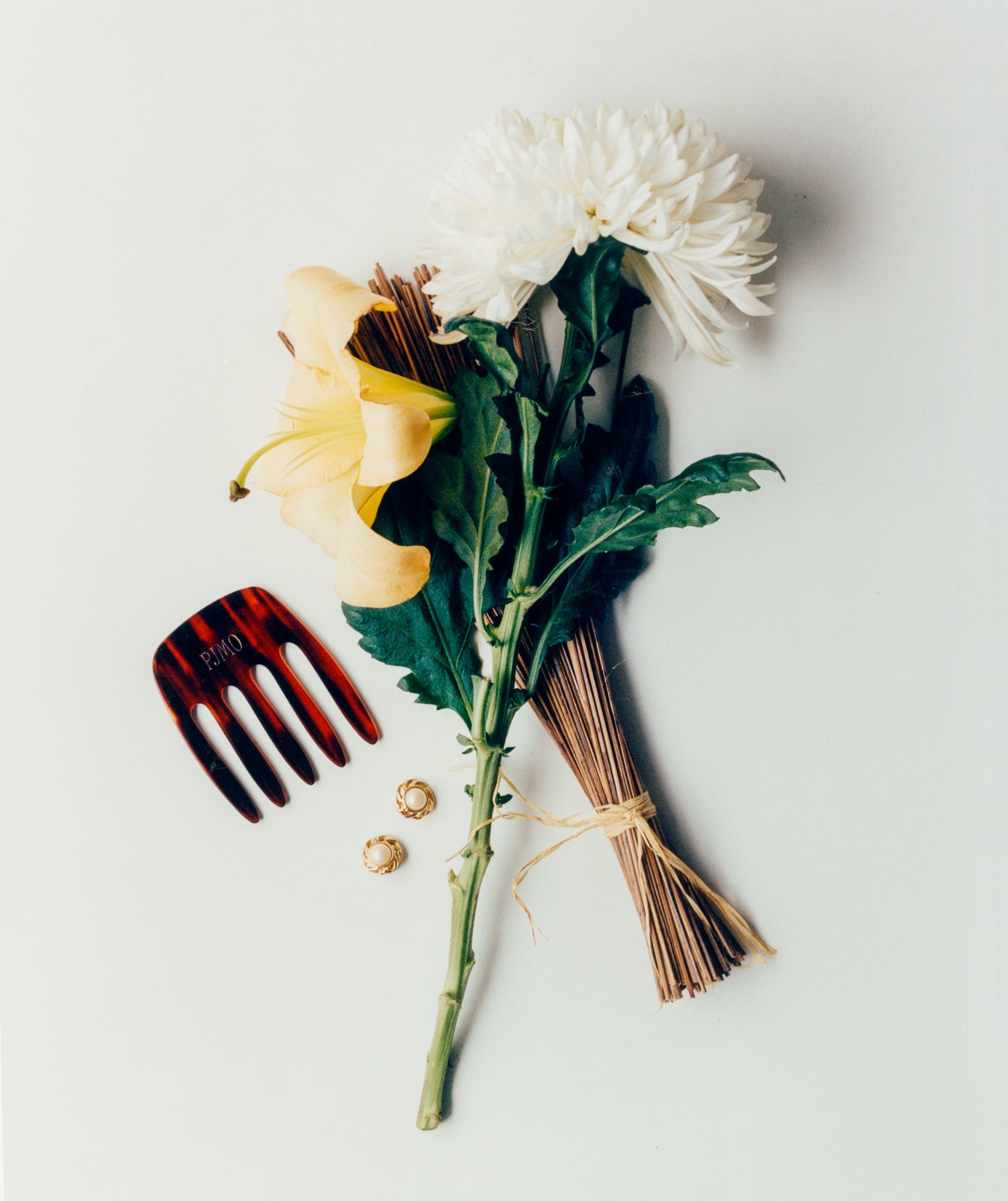 Liegendes Stillleben mit weißen und gelben Blumen, Räucherstäbchen, Schildpatt-Kamm und goldenen Ohrringen auf hellem Hintergrund