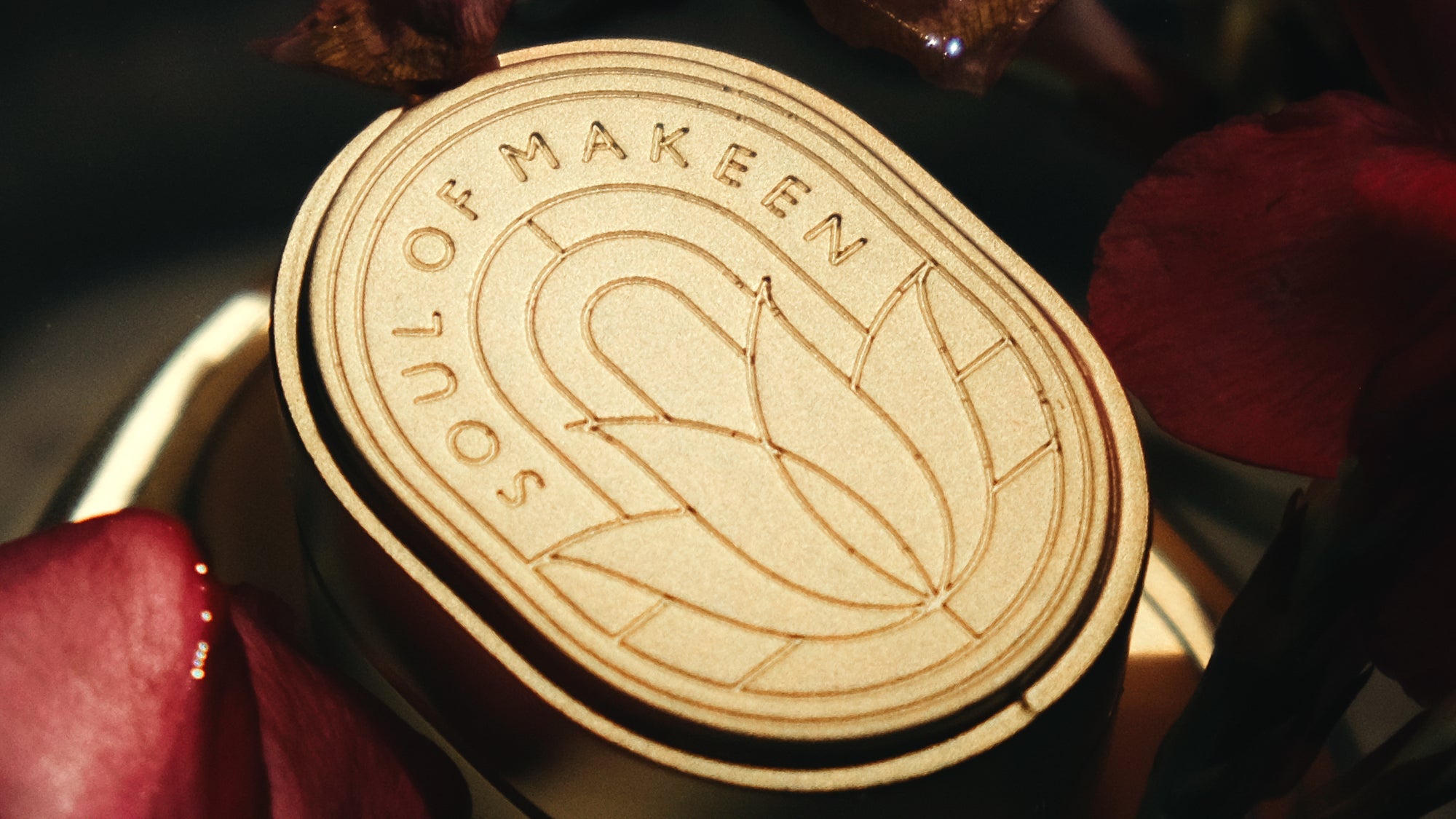 Nahaufnahme eines ovalen goldenen Metalldeckels mit graviertem Logo auf Parfumflakon aus Glas, dekoriert mit roten Blüten