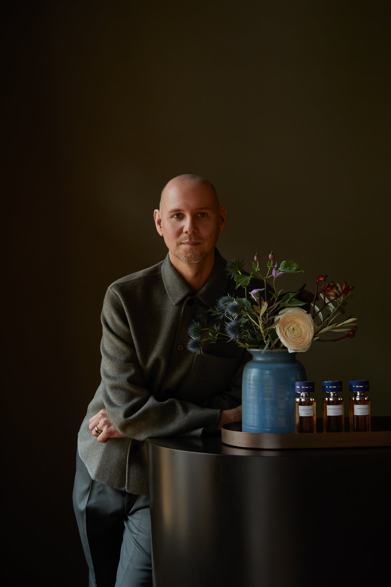 Gründer der Parfümerie 15West in Berlin in olivgrünem Hemd neben Tresen mit drei Parfumflakons mit blauen Deckeln und Vase mit Blumenarrangement